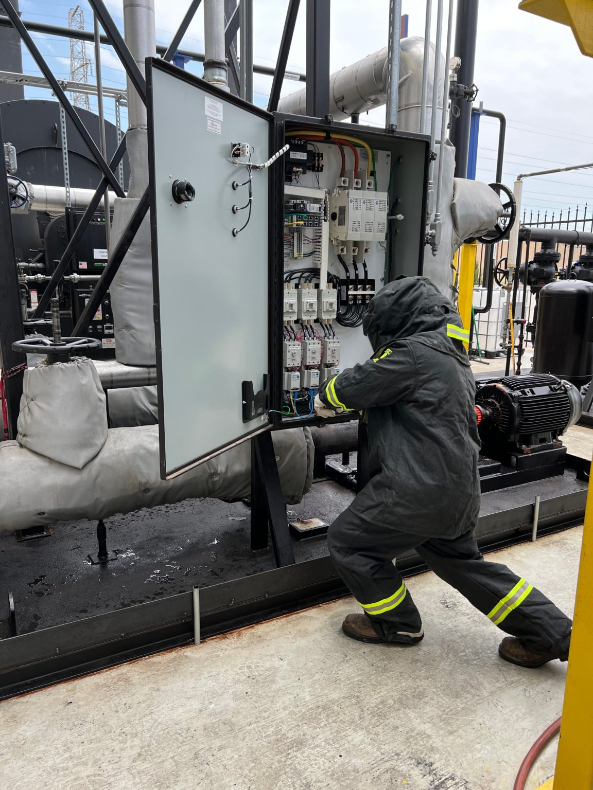 SIE electrician in arc-rated PPE working in an open control panel